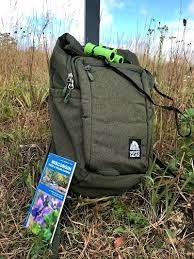 Dark green backpack sitting on the grass with a pair of bright green binoculars resting on top with a brochure leaning against it