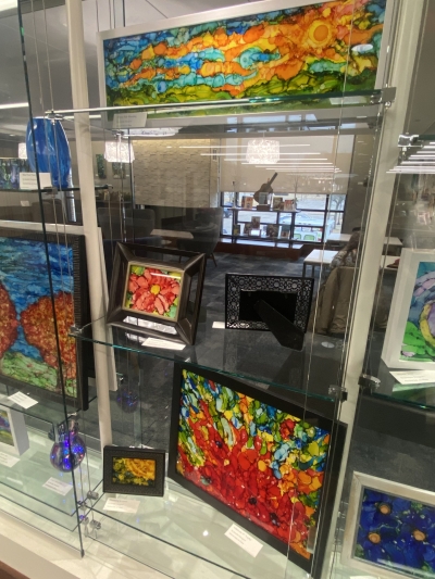 Display case with brightly colored alcohol ink paintings on glass.