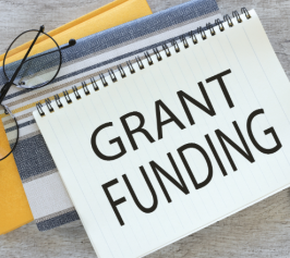 grant funding on a notepad laying on top of books with a pair of glasses