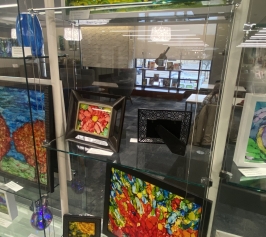 Display case with brightly colored alcohol ink paintings on glass.