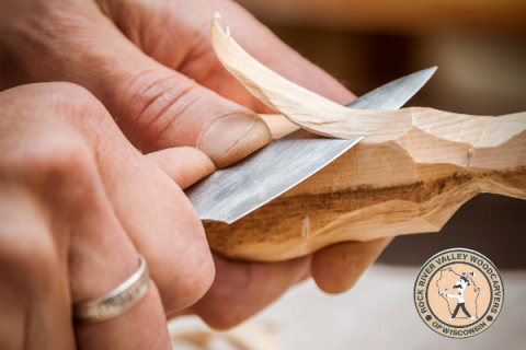 man's hands holding a knife and carving a piece of wood