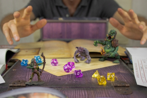 hands reaching over a dungeons and dragons board with colorful dice and small figurines