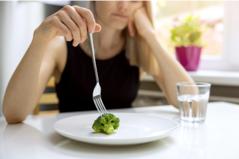 woman spearing a single piece of brocolli on a plate
