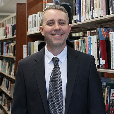 man in suit smiling in front of book shelves